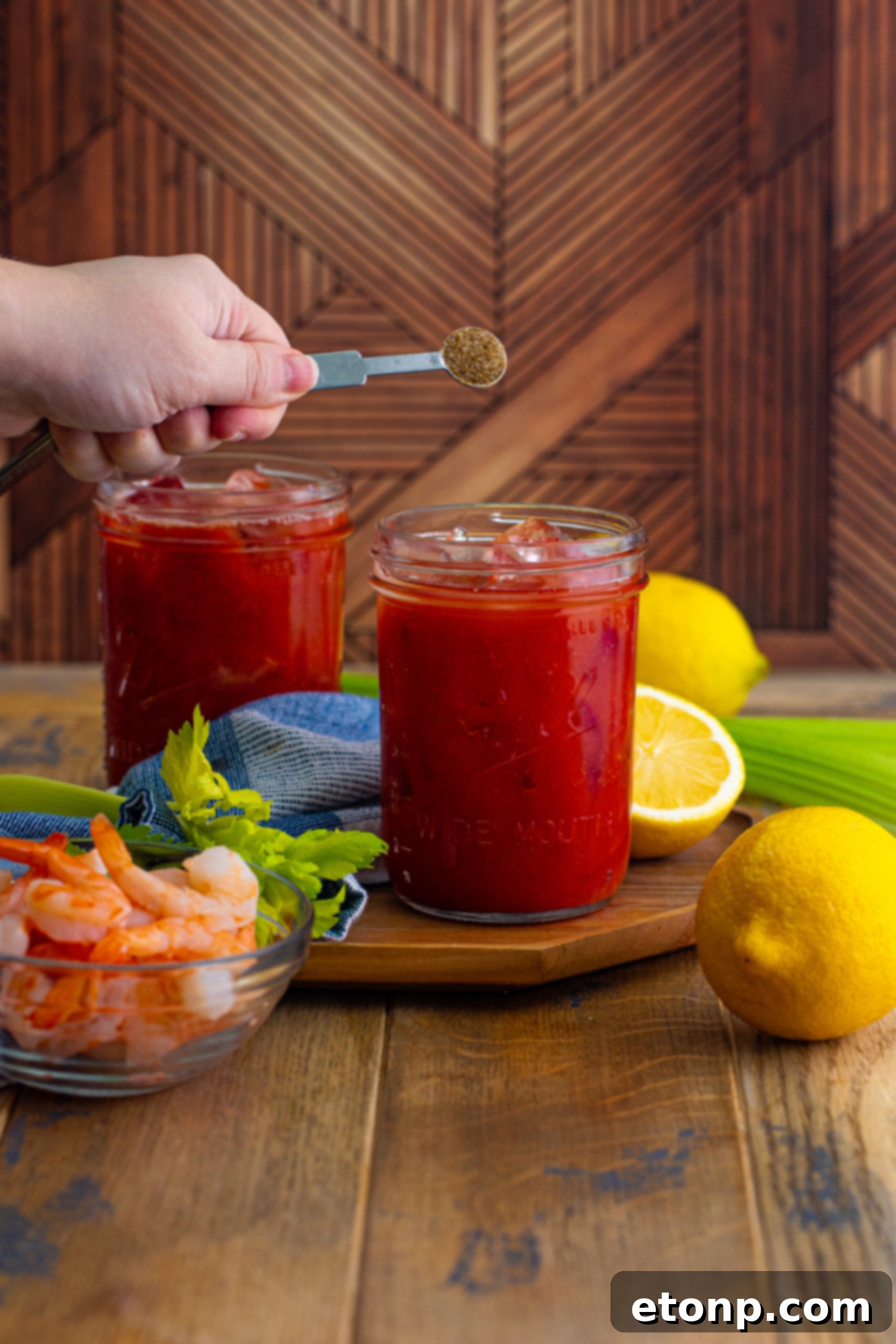 A measuring spoon delicately adding an ingredient into a Bloody Mary glass, ensuring precise flavor balance.