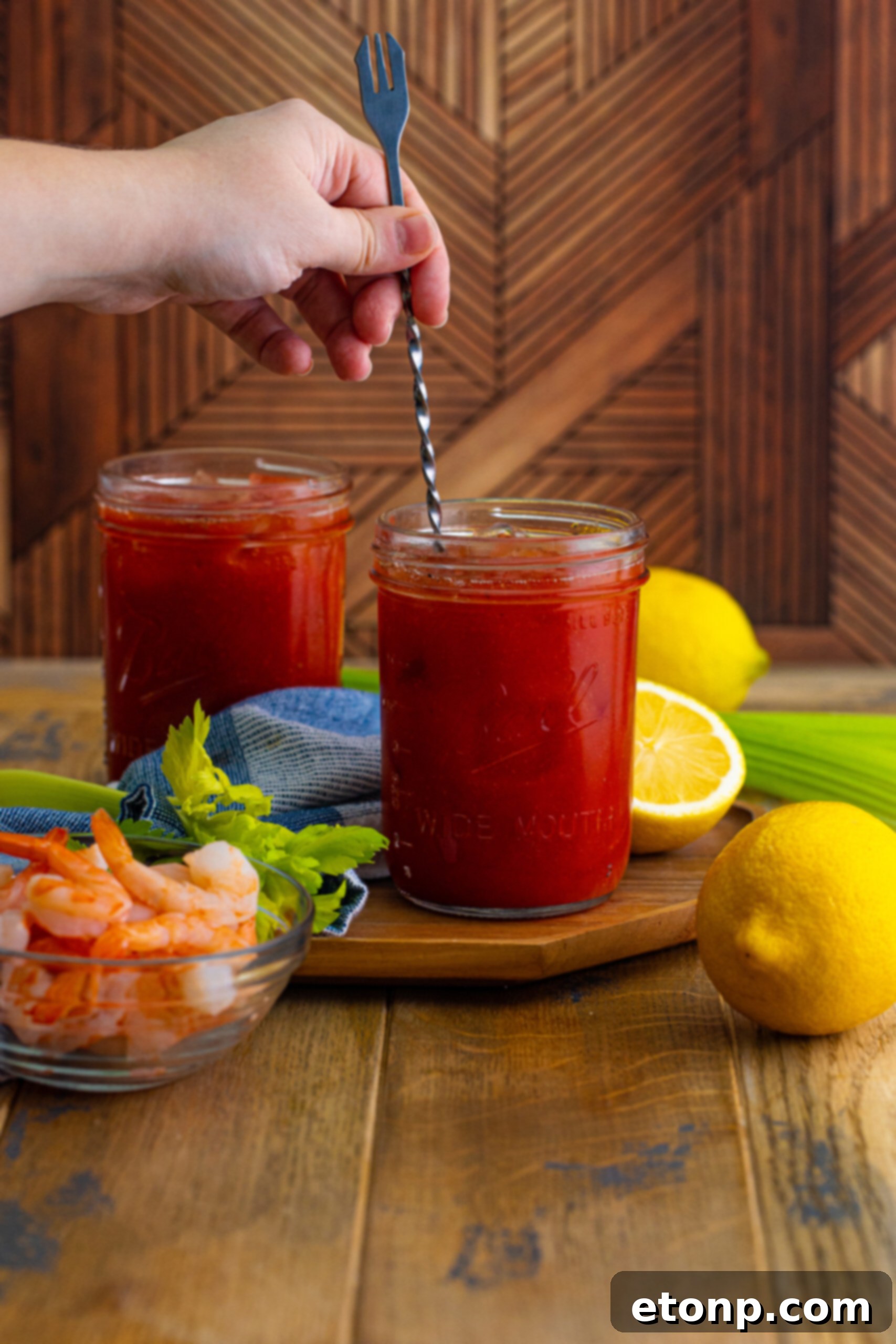 A hand stirring a Bloody Mary cocktail in a tall glass with a stir stick, blending all the flavors for a perfect mix.