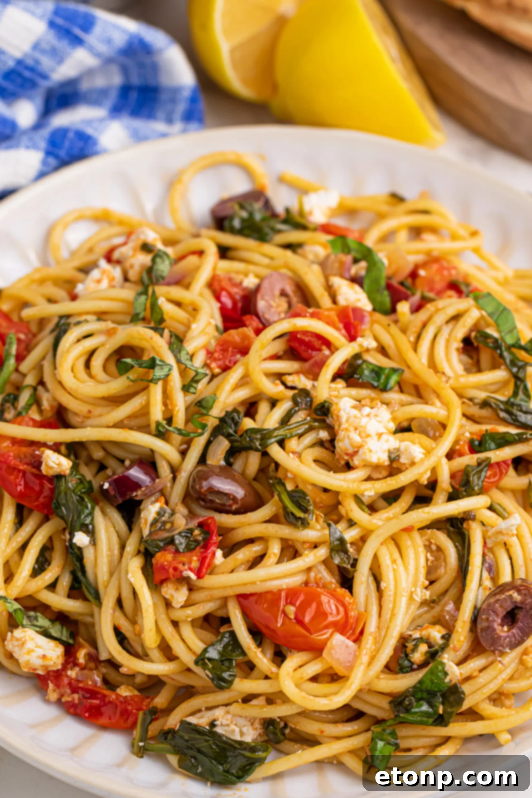 Close up shot of Greek Spaghetti on a white plate, showcasing the vibrant colors of tomatoes, olives, and feta
