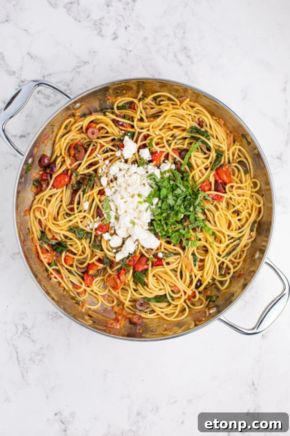 Finished Greek Spaghetti in a pan, garnished with crumbled feta cheese and fresh basil on top