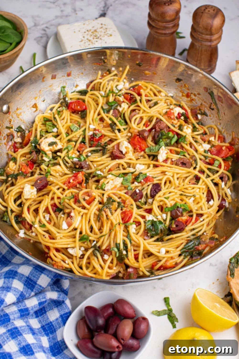 Greek Spaghetti artfully arranged in a pan, with Kalamata olives and sliced lemon garnishes beside it on the table
