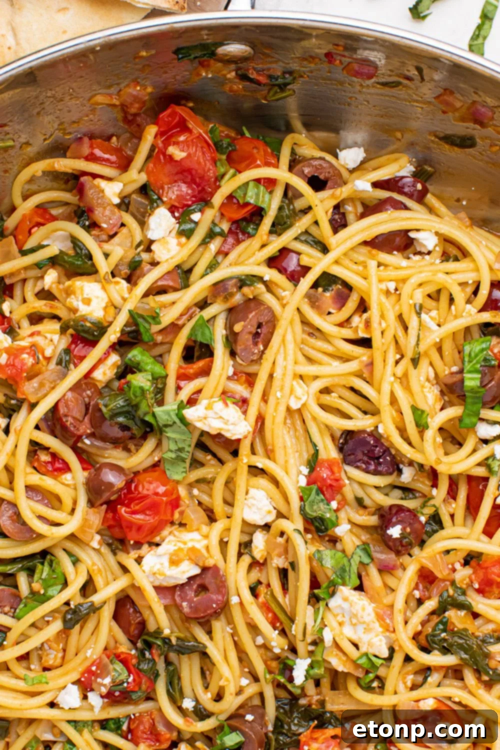 A close-up view of Greek Spaghetti in a pan, highlighting the intricate mix of pasta, vegetables, and feta cheese
