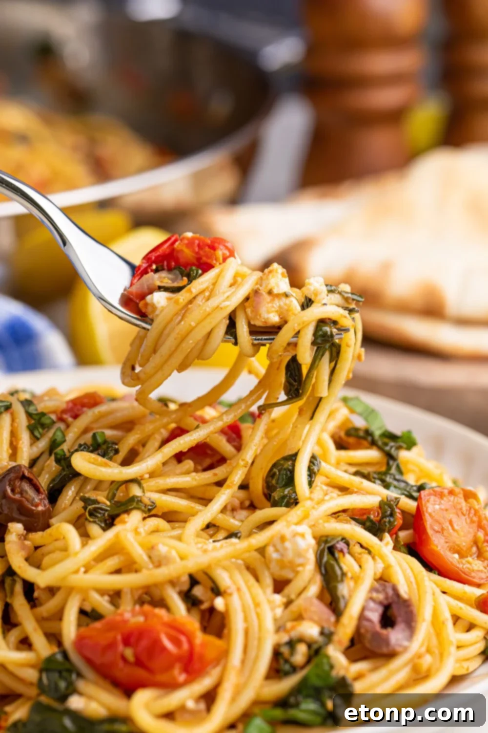 A fork lifting a delicious swirl of Greek Spaghetti above a plate, with salt and pepper shakers blurred in the background