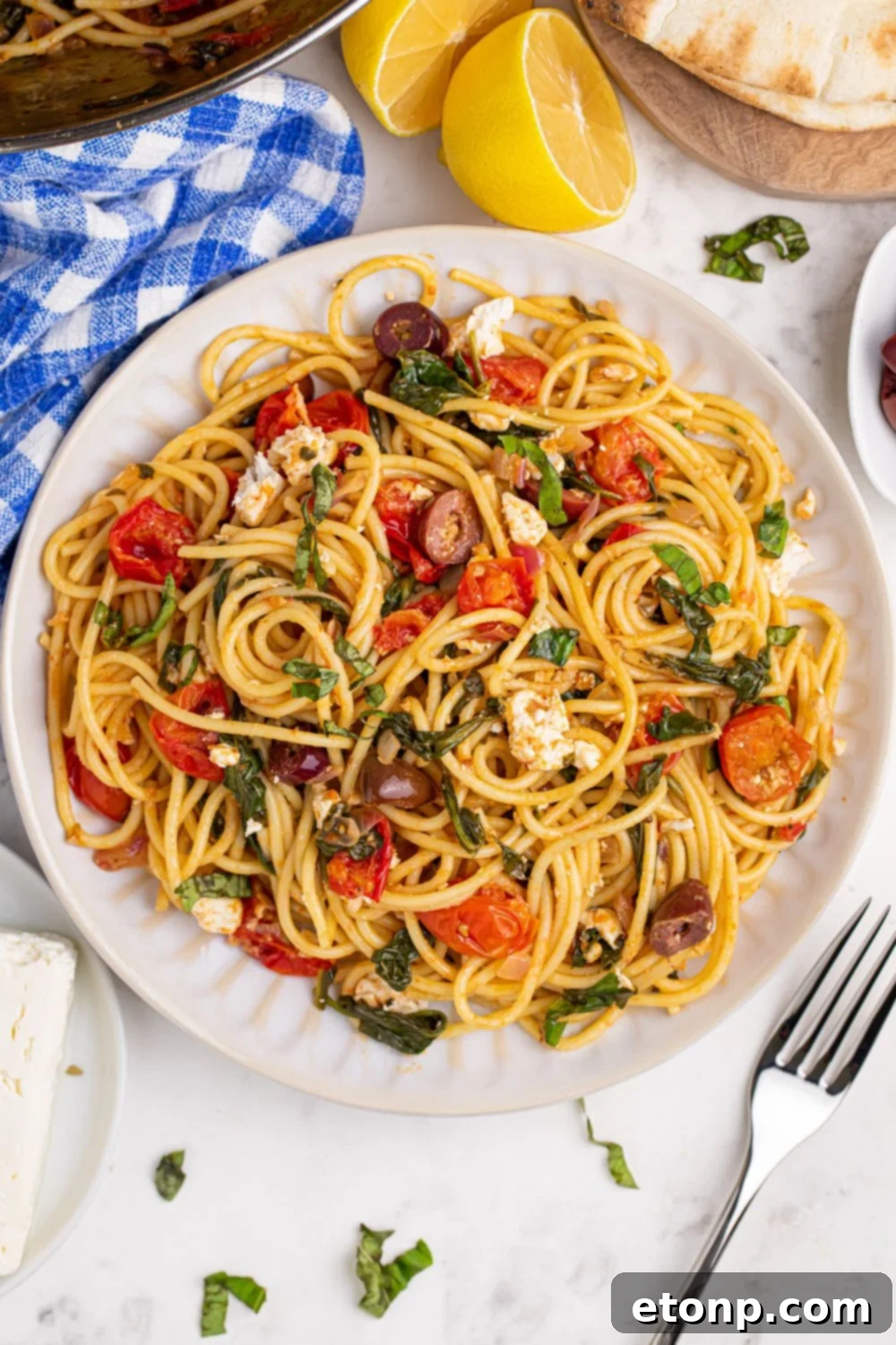 Greek Spaghetti beautifully plated with a linen towel and fork nearby, garnished with fresh lemon wedges
