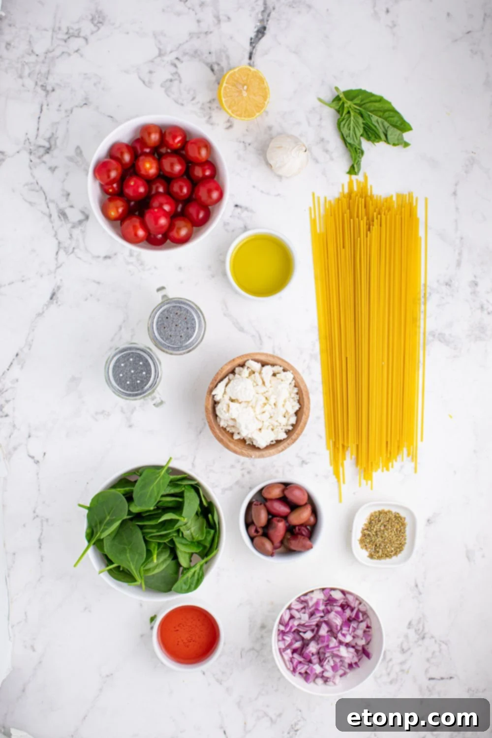 Greek Spaghetti ingredients laid out on a marble countertop, each in its own bowl, showcasing freshness and readiness for cooking