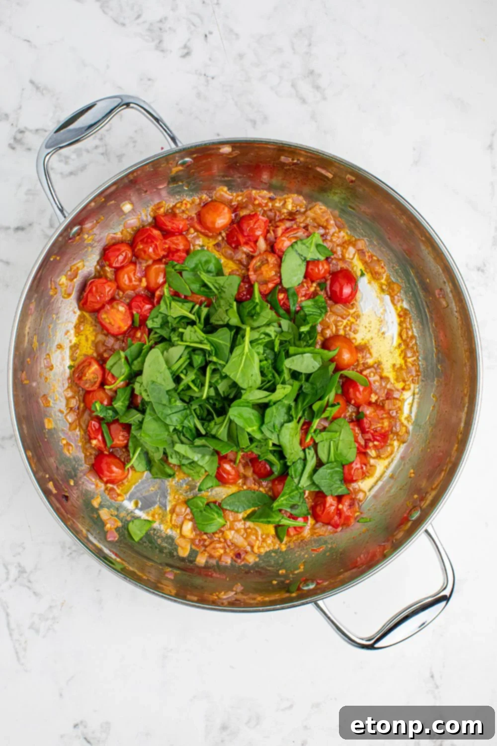 A pan with sautéed tomatoes and fresh basil leaves, fragrant and vibrant for the Greek Spaghetti