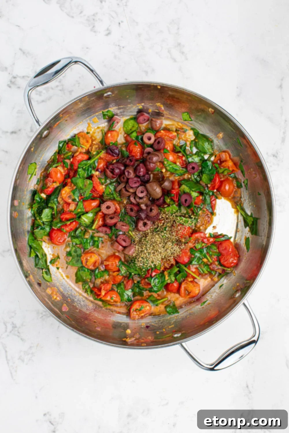 Mixed vegetables for Greek Spaghetti, including onions, garlic, and tomatoes, sautéing in a pan