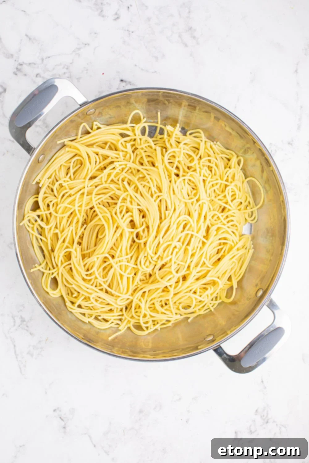 Cooked spaghetti noodles resting in a large pan, waiting to be combined with the Greek-inspired vegetable mixture