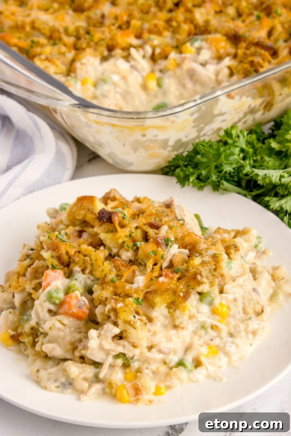 Chicken Stuffing Casserole on a plate with the pan behind it and fresh parsley on the side of pan 