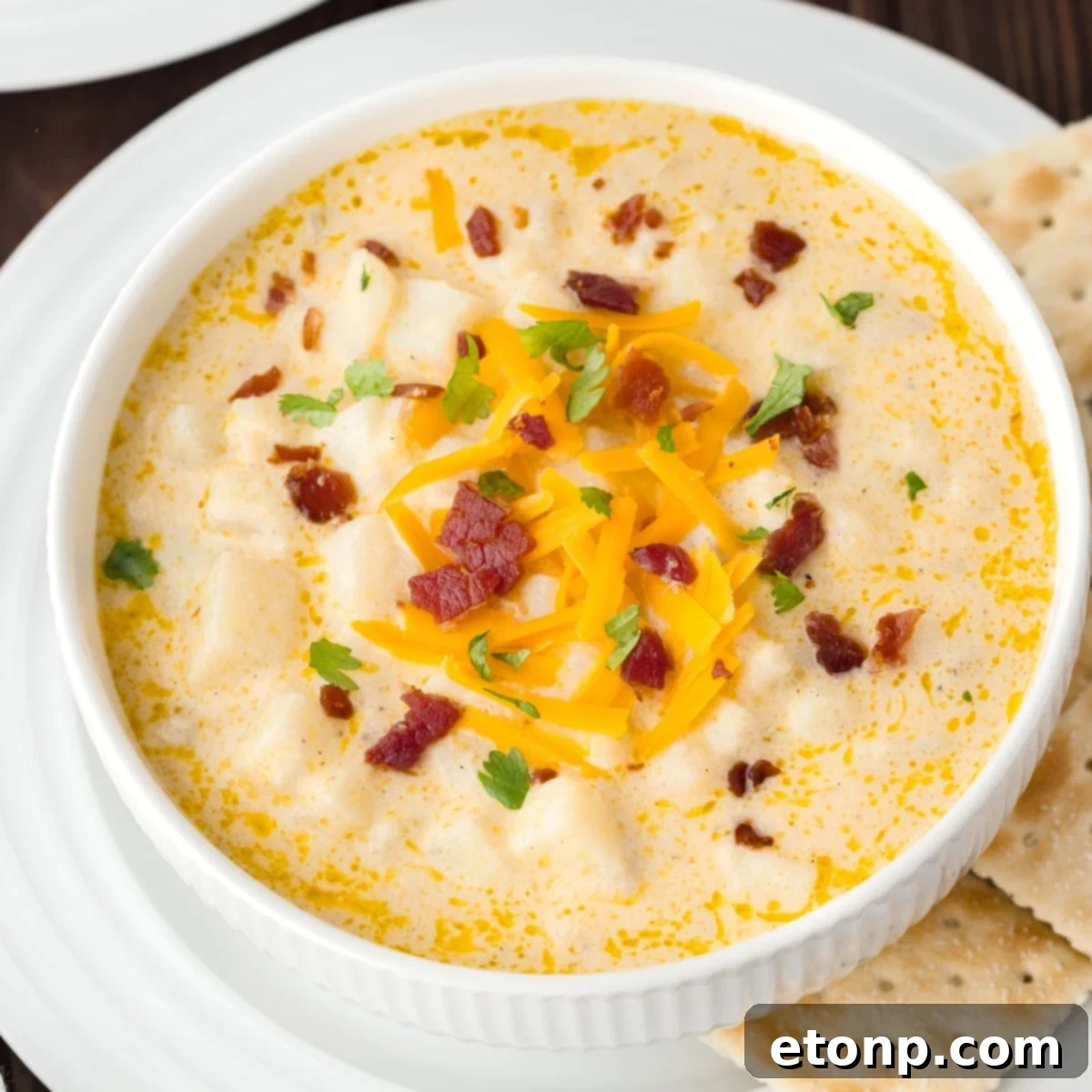 Hash Brown Potato Soup in a white bowl on a plate with saltine crackers on the side