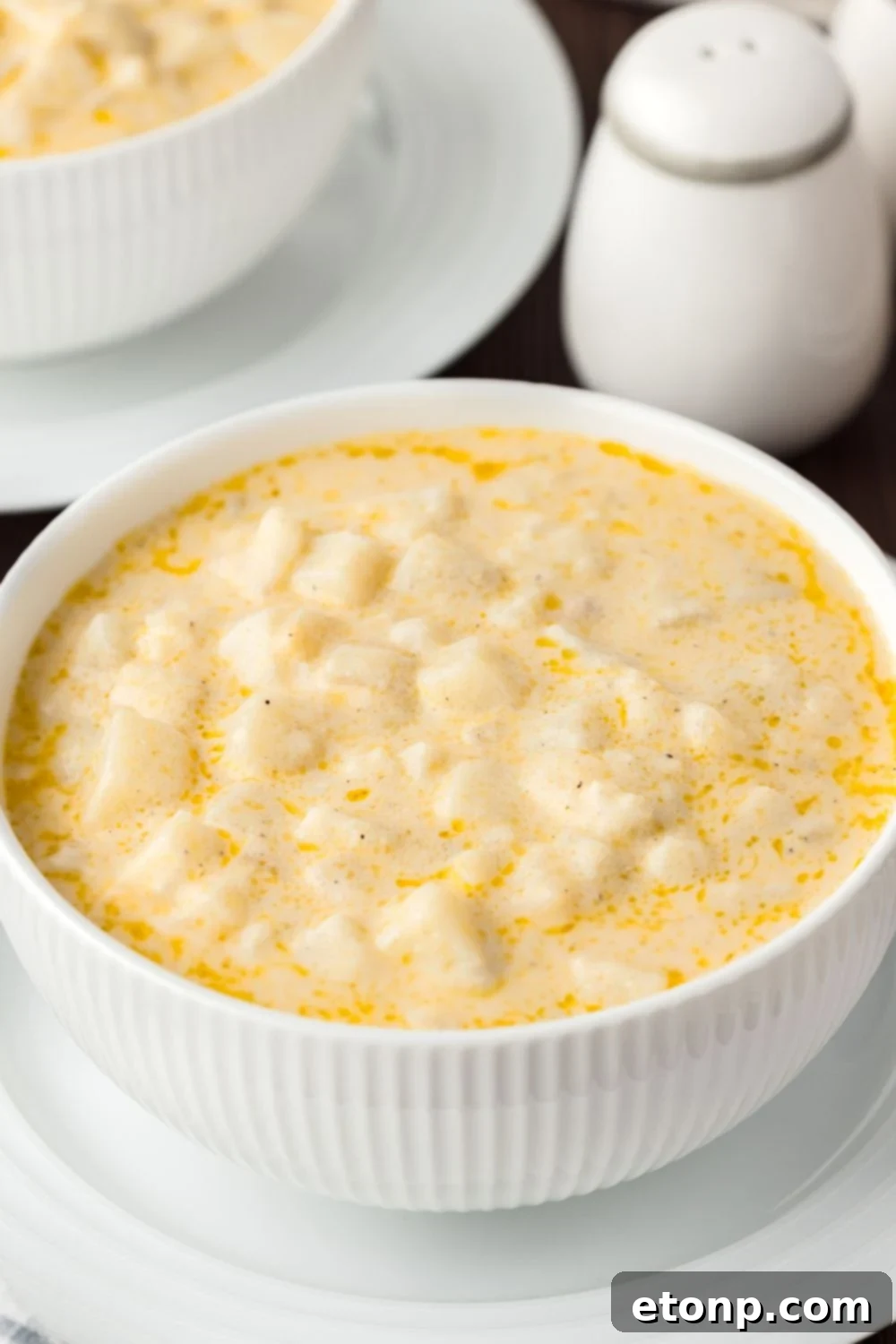 Hash Brown Potato Soup in a bowl with white dishes around the soup 