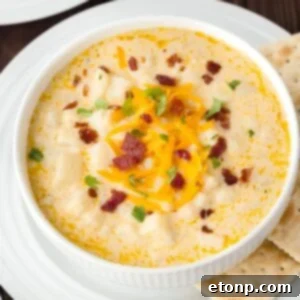 Hash Brown Potato Soup in a white bowl on a plate with saltine crackers on the side