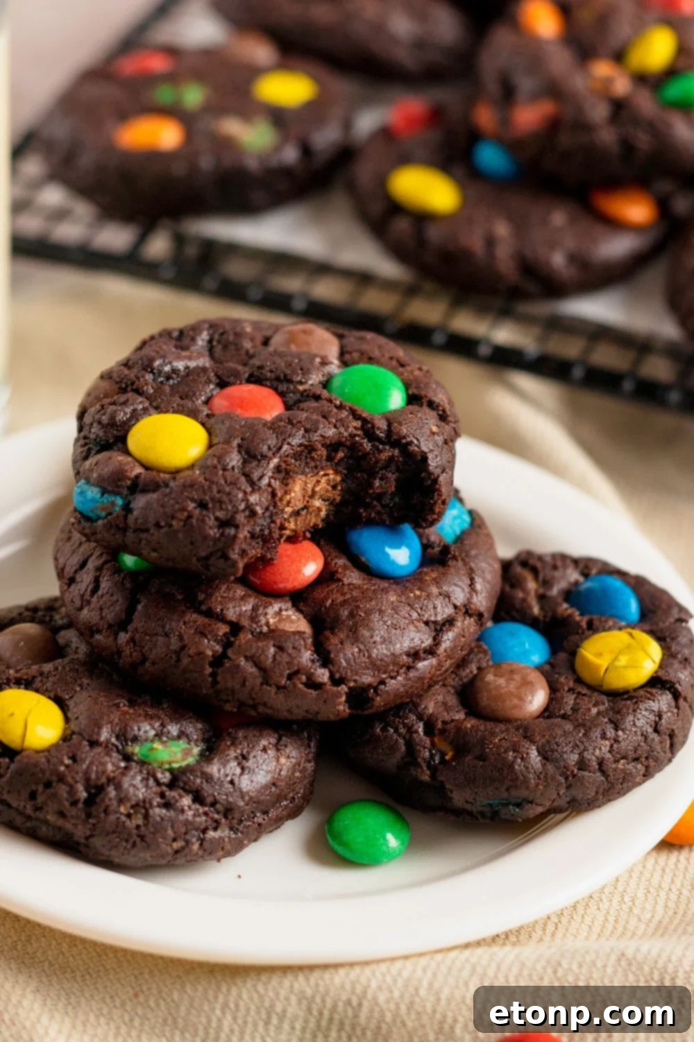 Chocolate M&M Cookies stacked on a white plate on table with a cookie with a bite taken out of it 