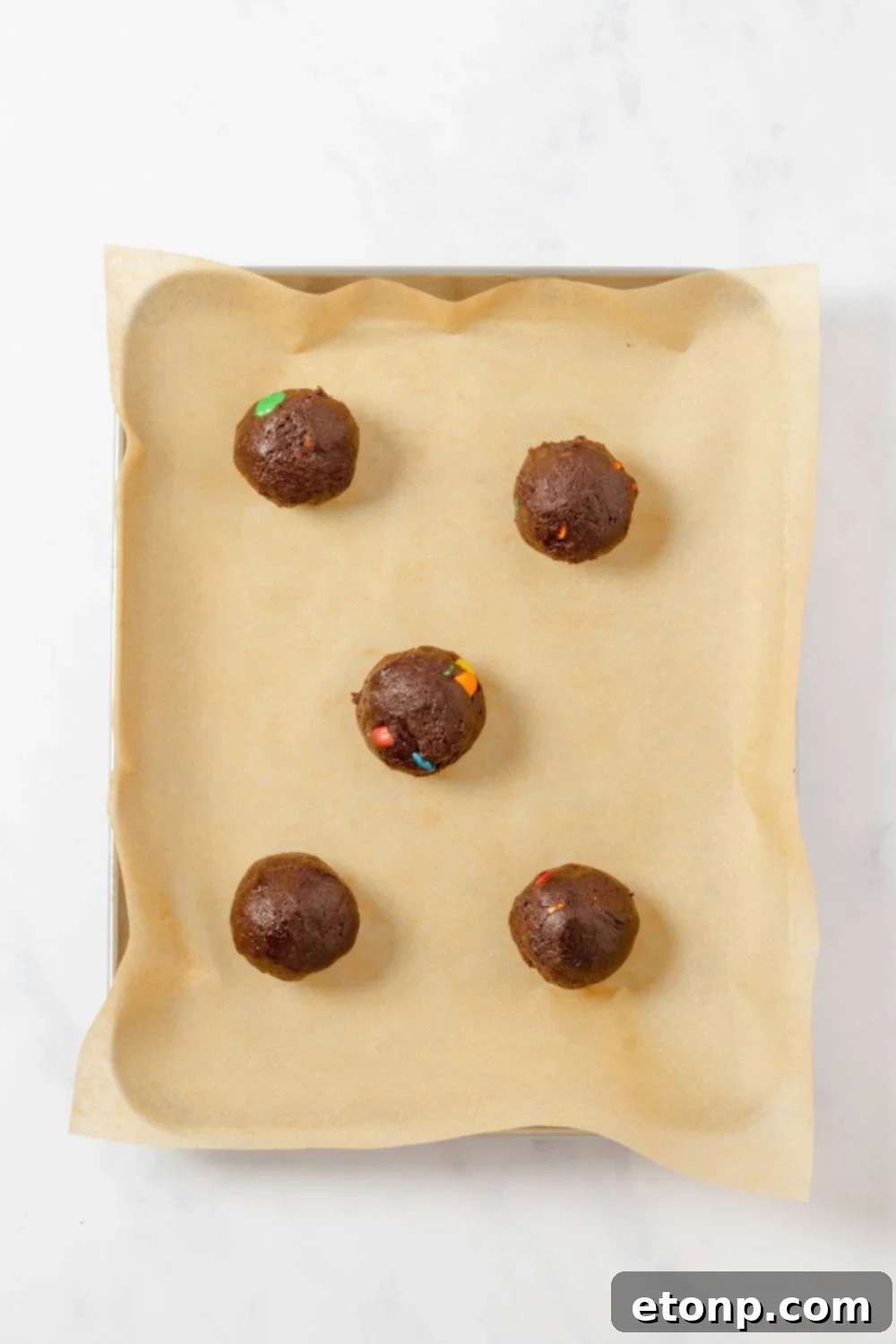Chocolate M&M Cookie dough balls on a lined cookie sheet 