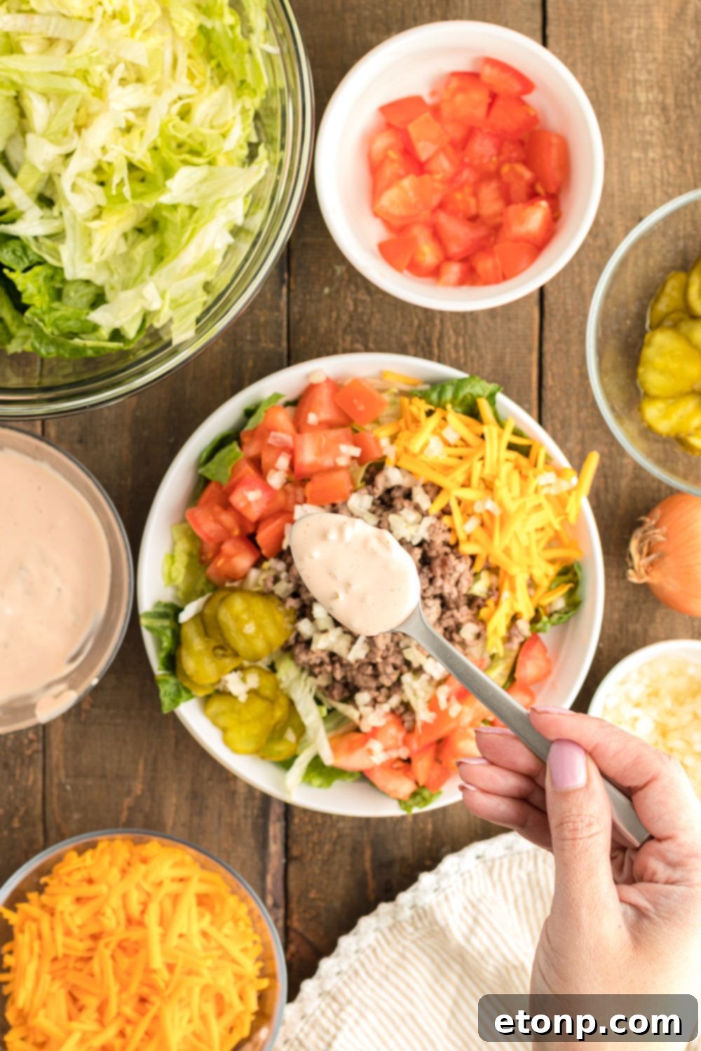 A small spoon drizzles the rich, creamy Big Mac Salad dressing over a freshly assembled salad in a bowl, highlighting the enticing final touch.