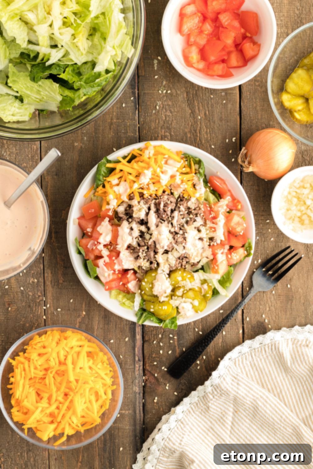 A comprehensive spread of Big Mac Salad components, with the main salad bowl surrounded by individual bowls of fresh ingredients like lettuce, ground beef, cheese, and dressing, all on a wooden table.