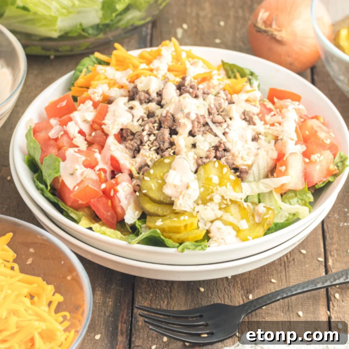 Close-up view of Big Mac Salad in a rustic bowl on a wooden table, with various ingredients like fresh lettuce, ground beef, and cheese visible. A fork is poised, ready for a delicious bite.