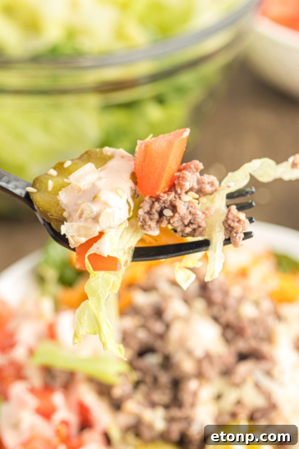 A fork lifts a generous portion of Big Mac Salad from a bowl, showcasing the rich layers of ground beef, cheese, lettuce, and the creamy secret sauce, ready to be enjoyed.