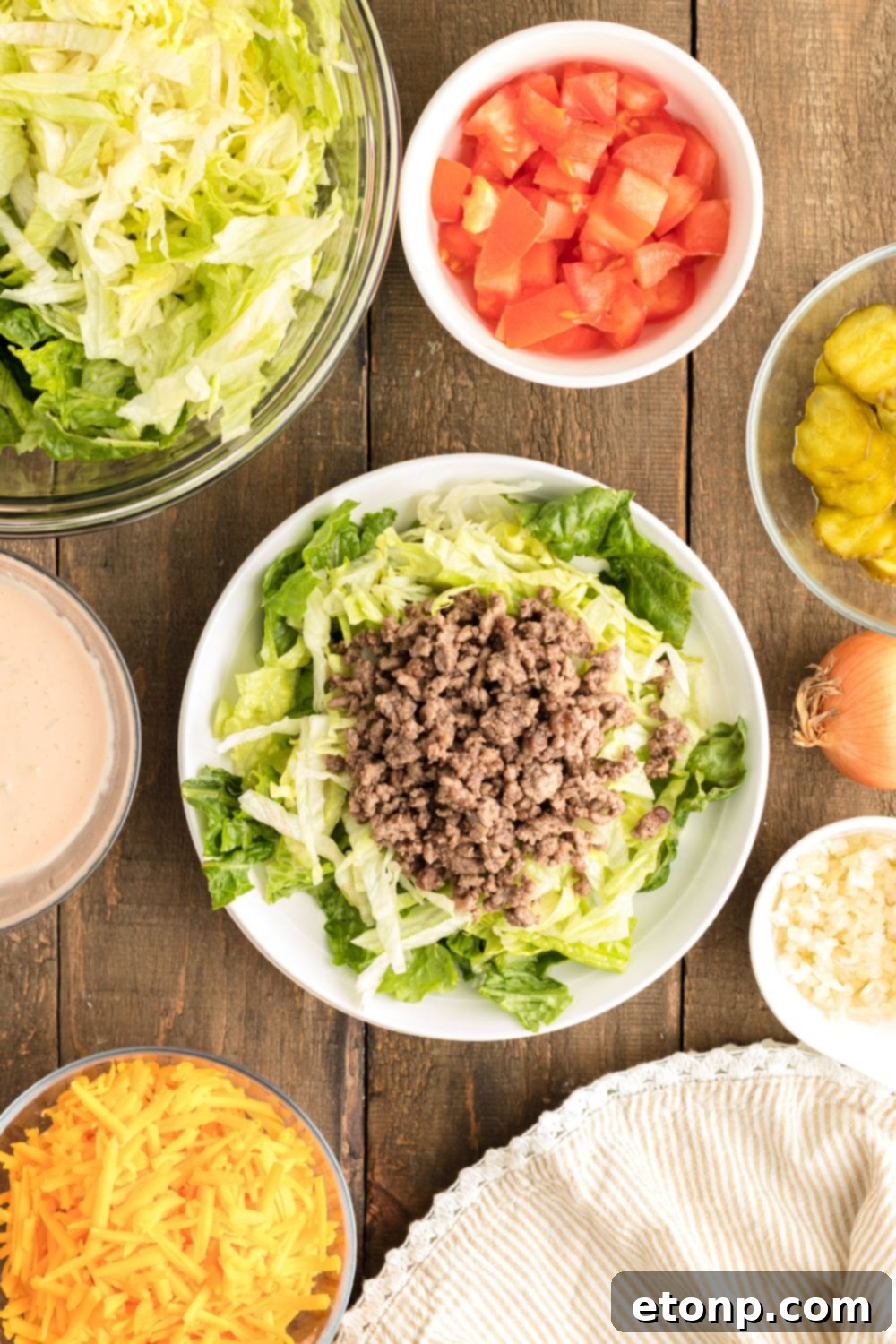 A partially assembled Big Mac Salad on a plate, featuring a layer of fresh lettuce topped with seasoned ground beef, ready for more delicious additions.