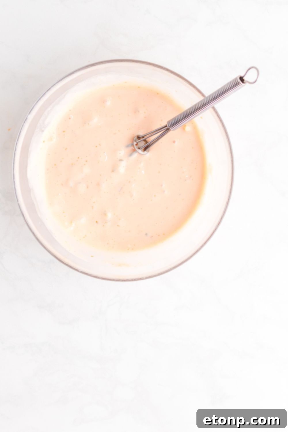 The Big Mac Salad dressing, a creamy and tangy mixture, is perfectly blended in a glass bowl with a whisk resting beside it, ready to be added to the salad.