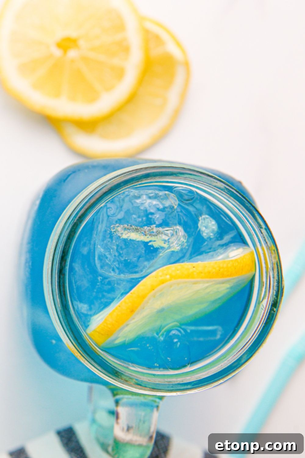 An overhead view of a glass filled with Blue Raspberry Lemonade, with a few lemon slices scattered on the table.