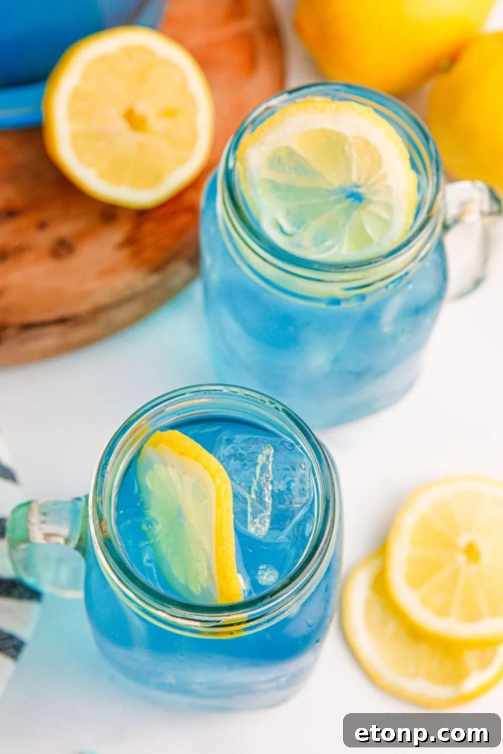 Two glasses of Blue Raspberry Lemonade, with fresh lemons and a wooden cutting board in the background on a rustic table.
