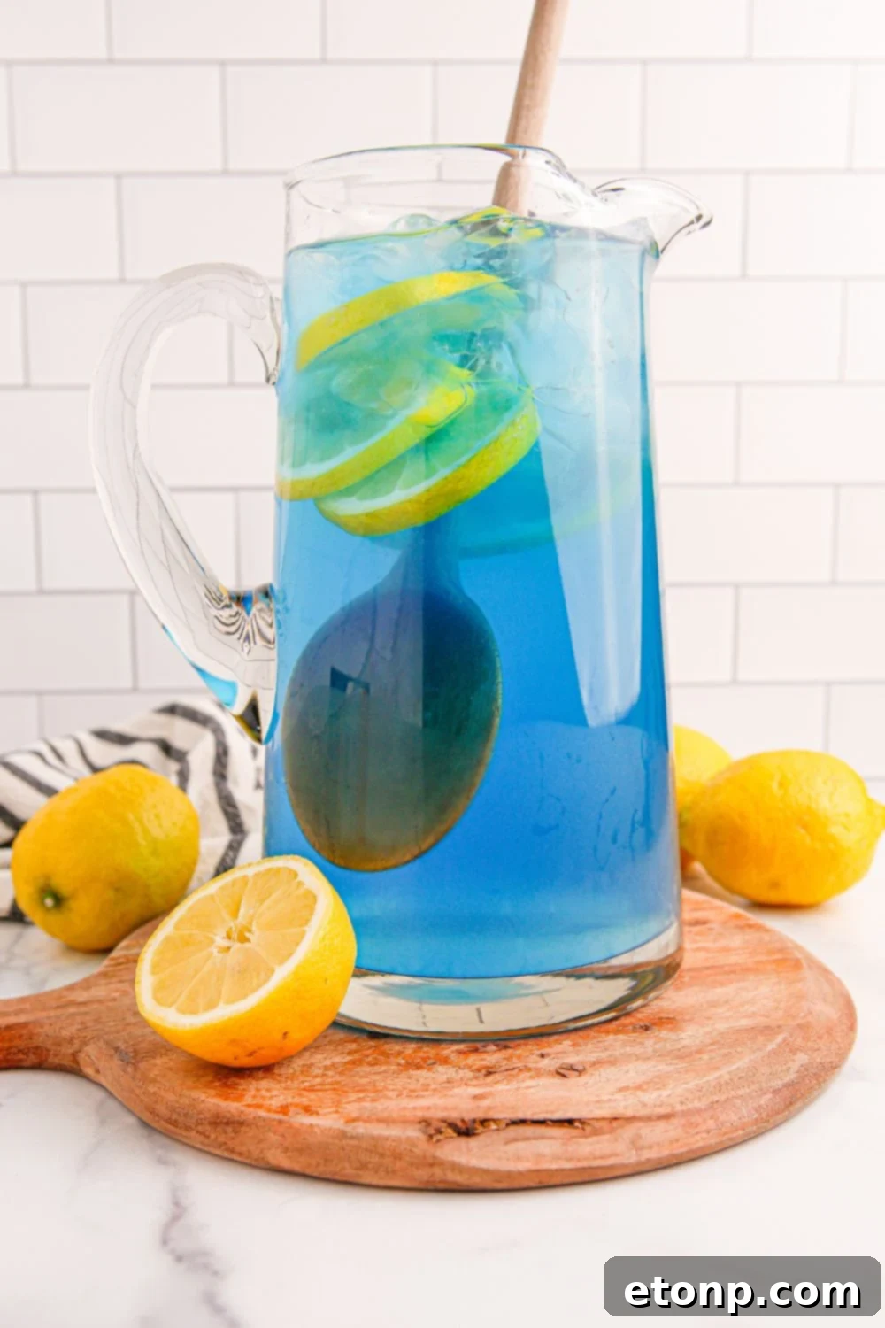 A pitcher of Blue Raspberry Lemonade with a stirring spoon inside, ready to be served.
