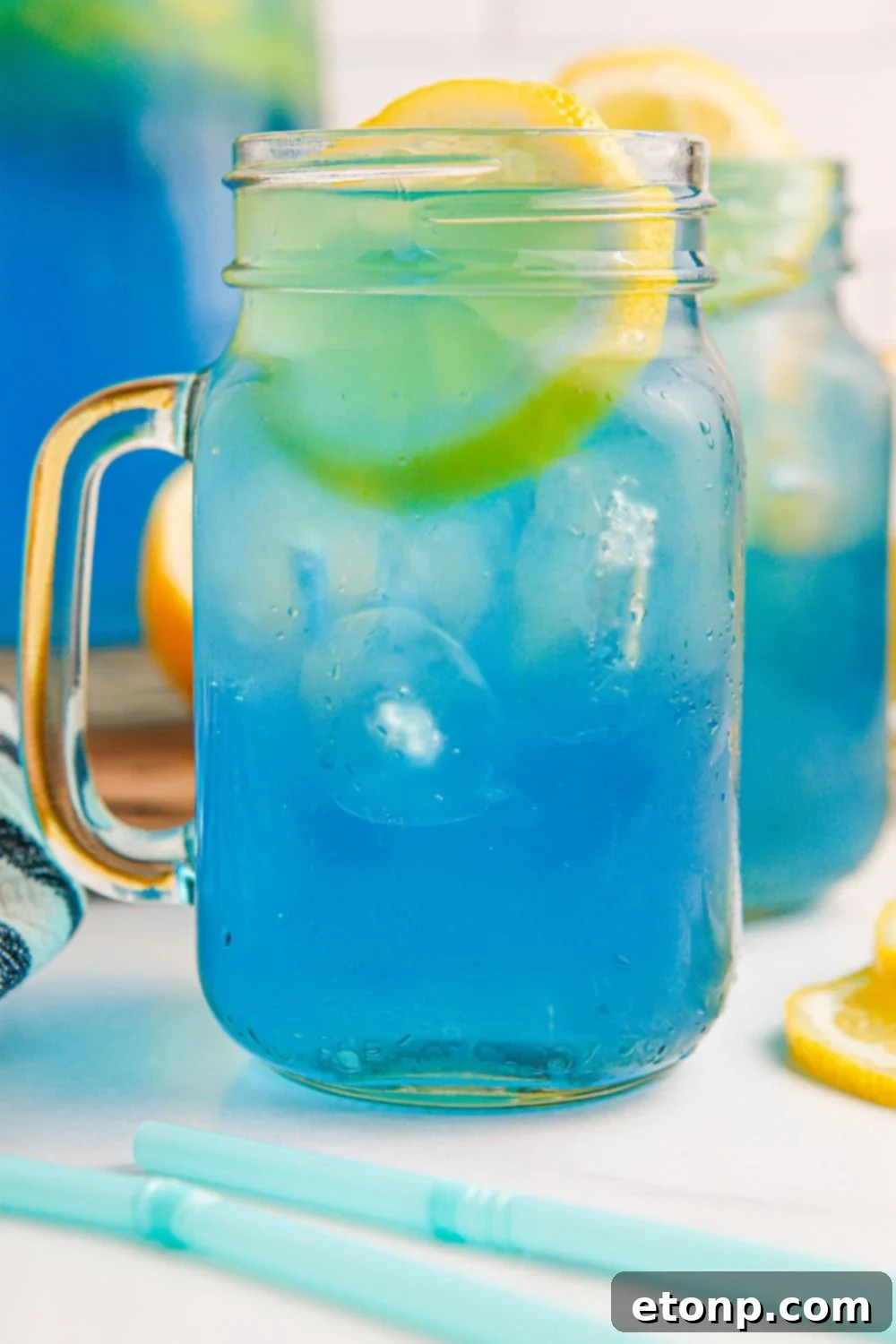 Close-up of Blue Raspberry Lemonade served in mason jars on a table, with straws indicating it's ready for enjoyment.
