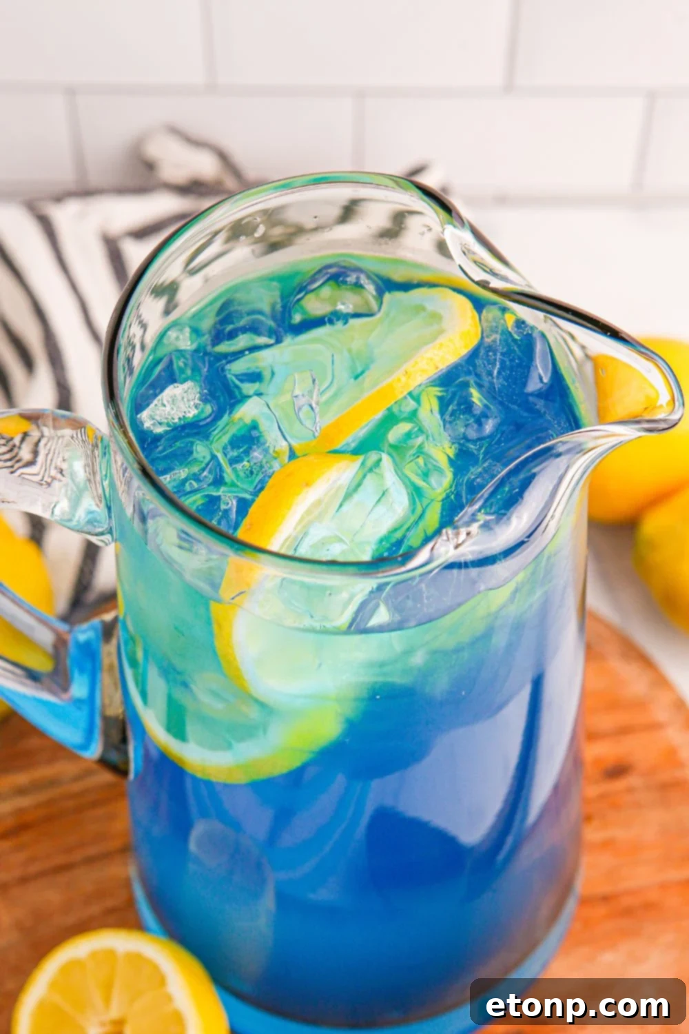 A completed pitcher of Blue Raspberry Lemonade, chilling on a table with a rustic towel draped behind it, awaiting serving.