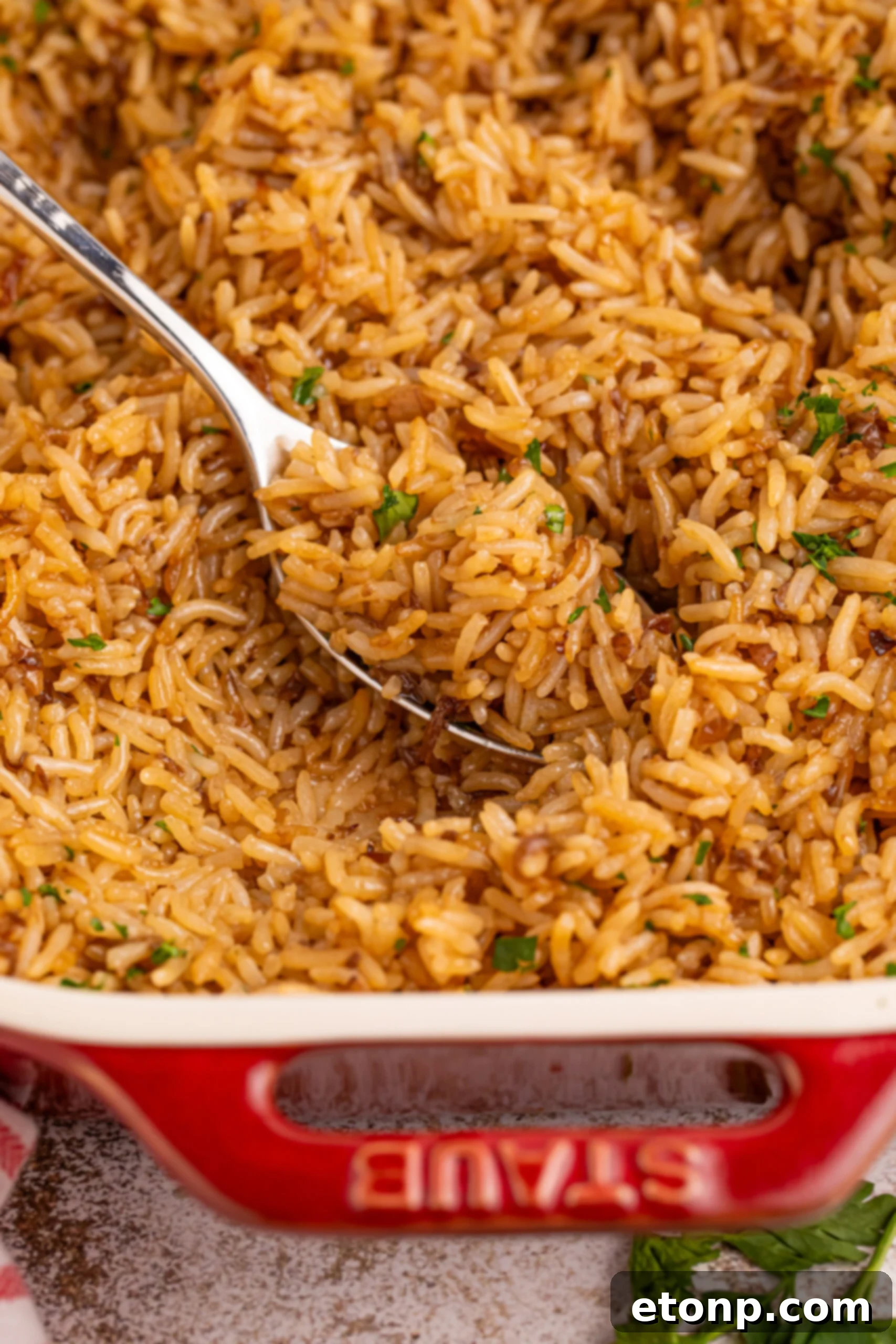 A close-up of French Onion Soup Rice in a vibrant red baking dish, with a spoonful being lifted to show its buttery, flavorful texture.