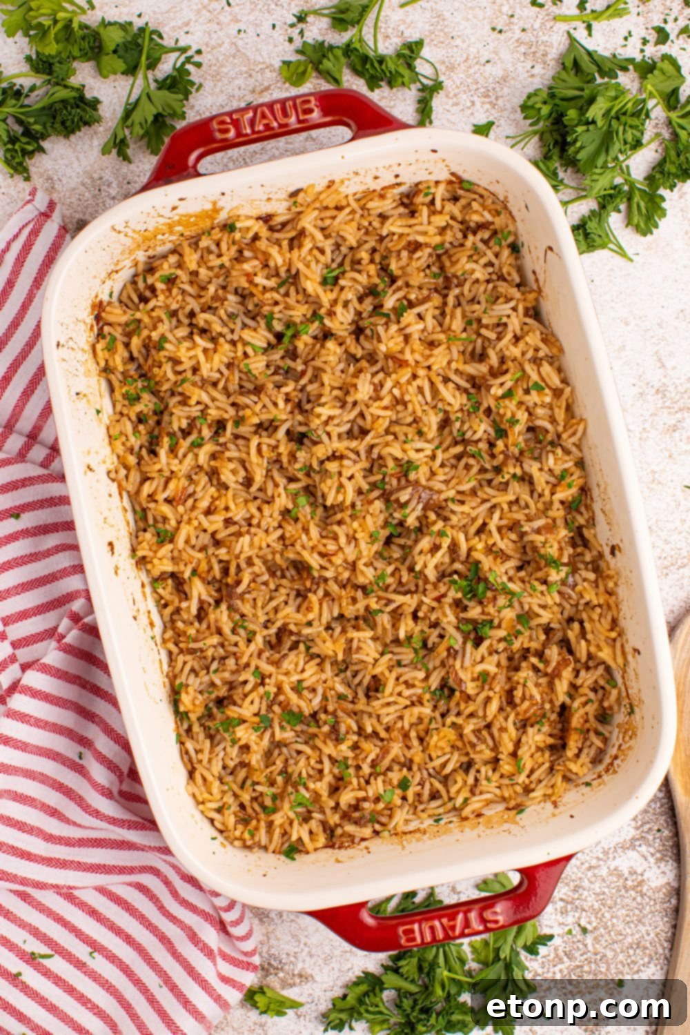 Baked Stick of Butter Rice in a casserole dish, garnished with fresh parsley and resting on a table with a kitchen towel.