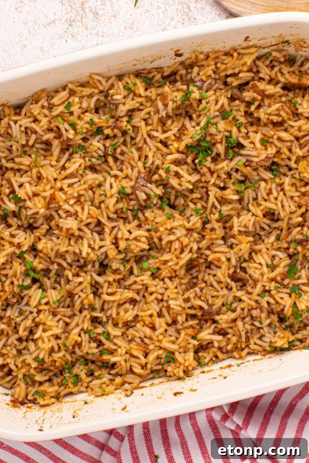 Baked Stick of Butter Rice in a casserole pan, sitting on a wooden table with a red kitchen towel underneath.