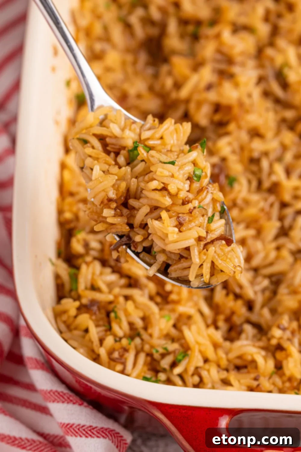 A casserole dish of Stick of Butter Rice with a serving spoon lifting a generous scoop of fluffy rice.