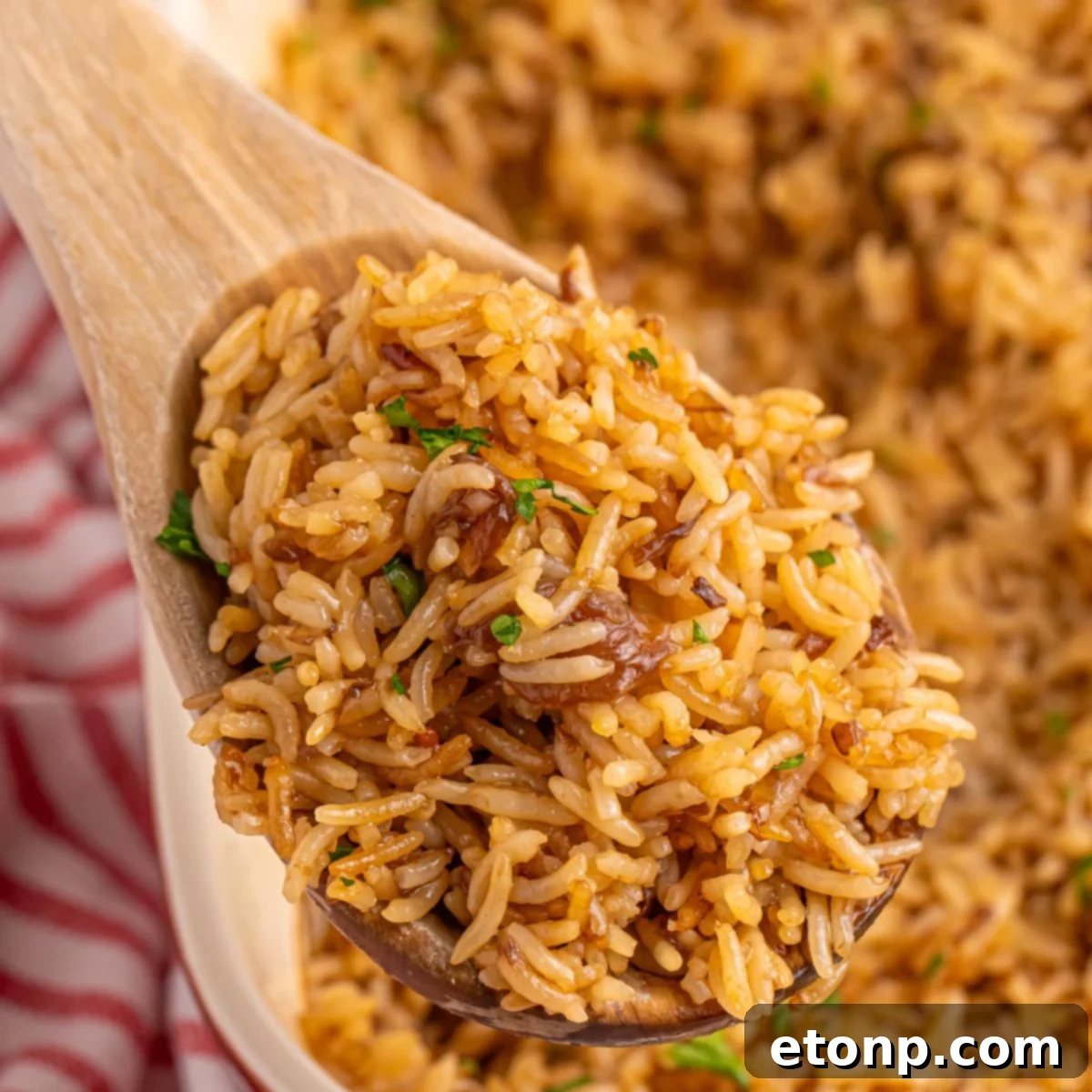 Stick of Butter Rice served in a pan on a rustic wooden table, with a wooden spoon holding a fluffy portion of rice.
