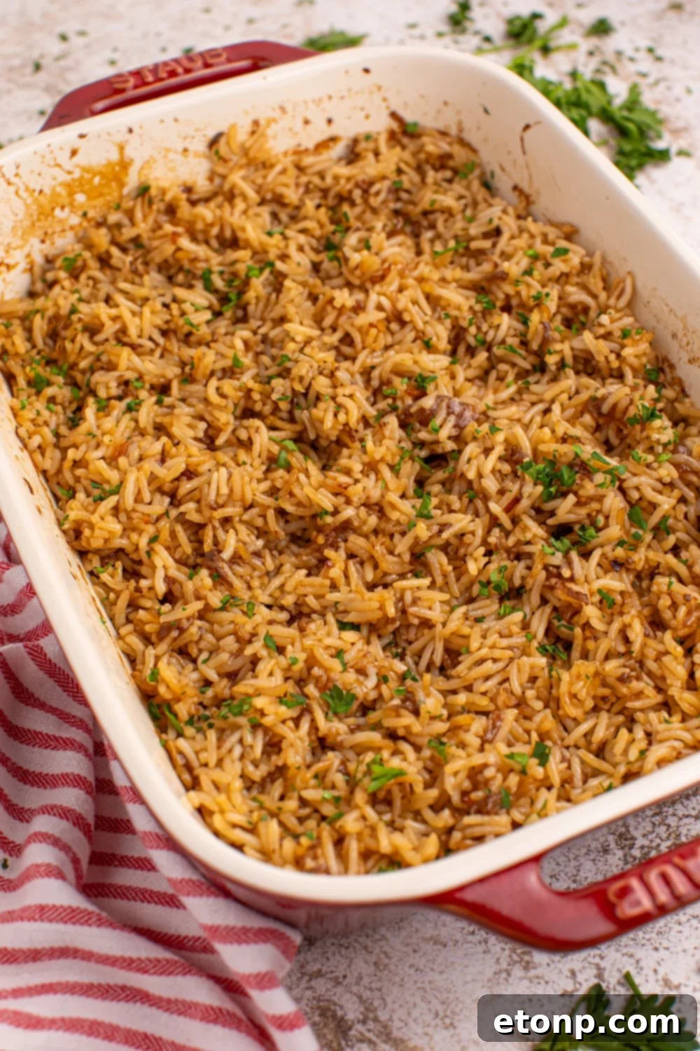 A pan of cooked Stick of Butter Rice, fluffy and golden, resting on a table with a red striped towel beside it.