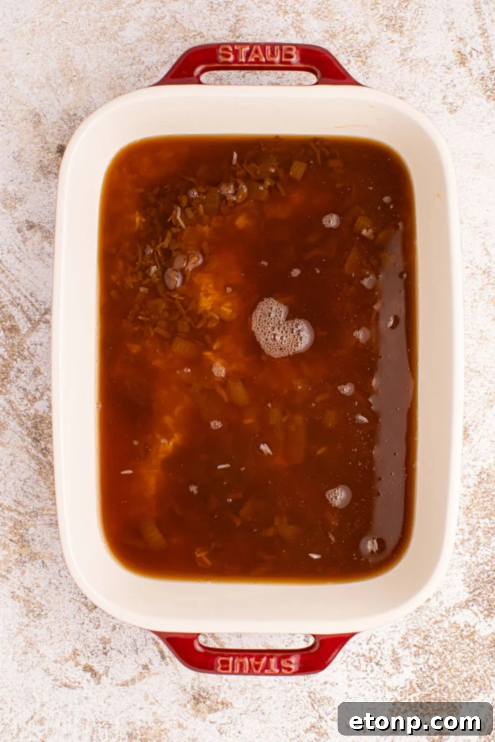 A casserole dish containing the Stick of Butter Rice mixture with rice, beef broth, and French onion soup combined.
