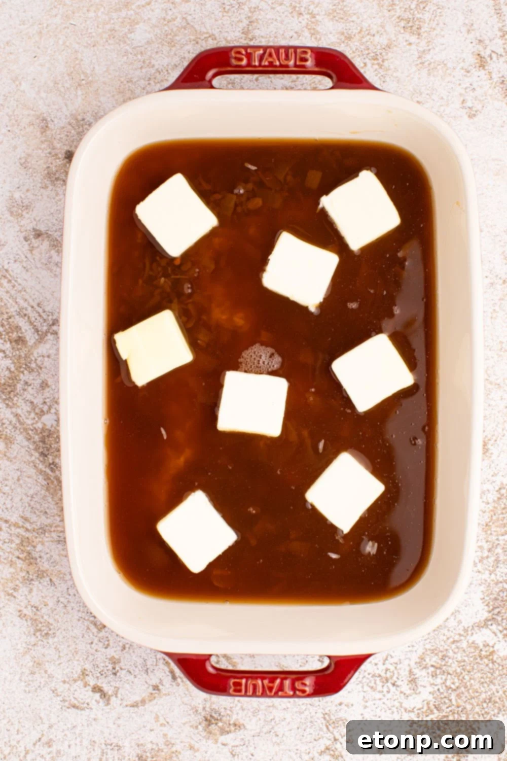 Slabs of unsalted butter evenly distributed on top of the Stick of Butter Rice mixture in a casserole dish, ready for baking.
