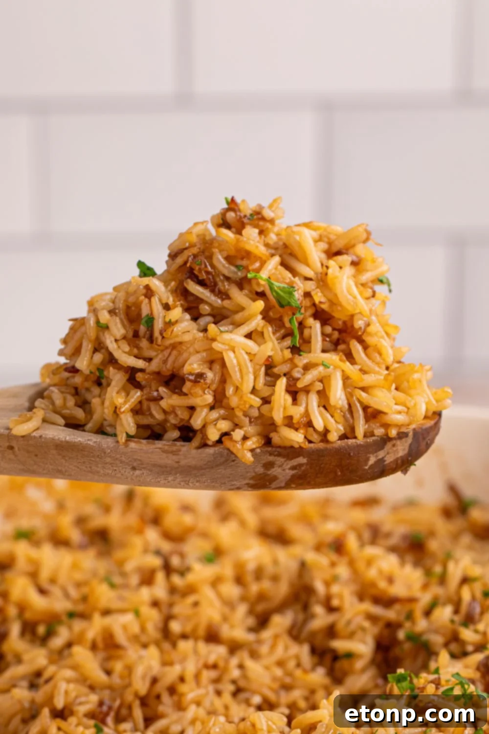 A wooden spoon lifting a scoop of fluffy Stick of Butter Rice above the pan, showcasing its texture.