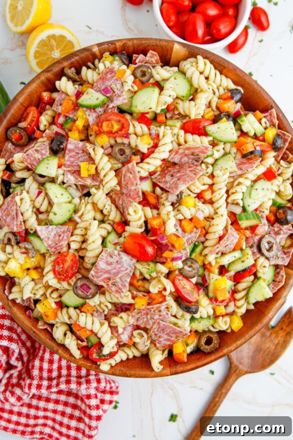Vibrant Summer Pasta Salad 17 Summer Pasta Salad in a bowl with spoon beside it and tomatoes and lemons on the side of bowl