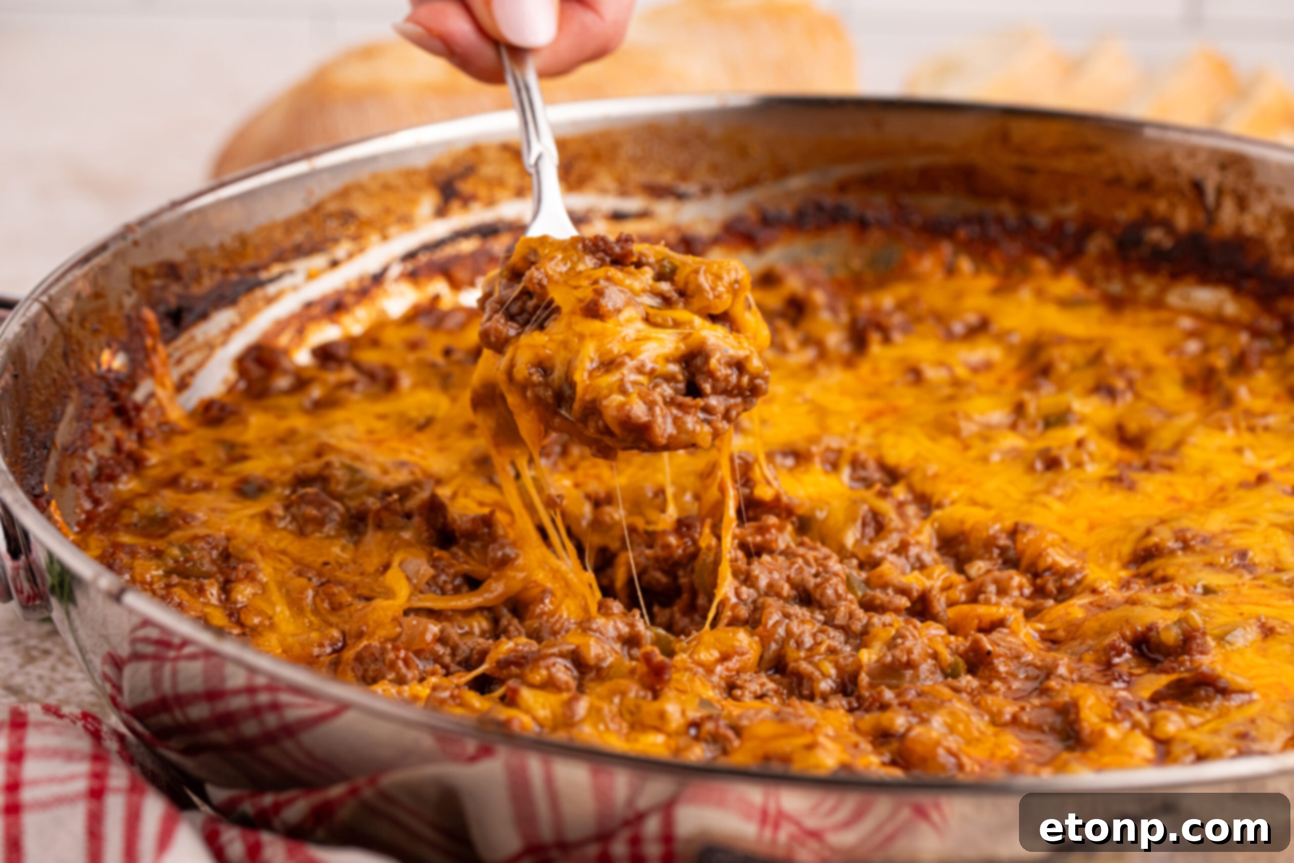 Ultimate Sloppy Joe Dip 10 A close-up shot of a spoon scooping a generous portion of cheesy Sloppy Joe Dip from a silver pan, showing its enticing texture and melted cheese.