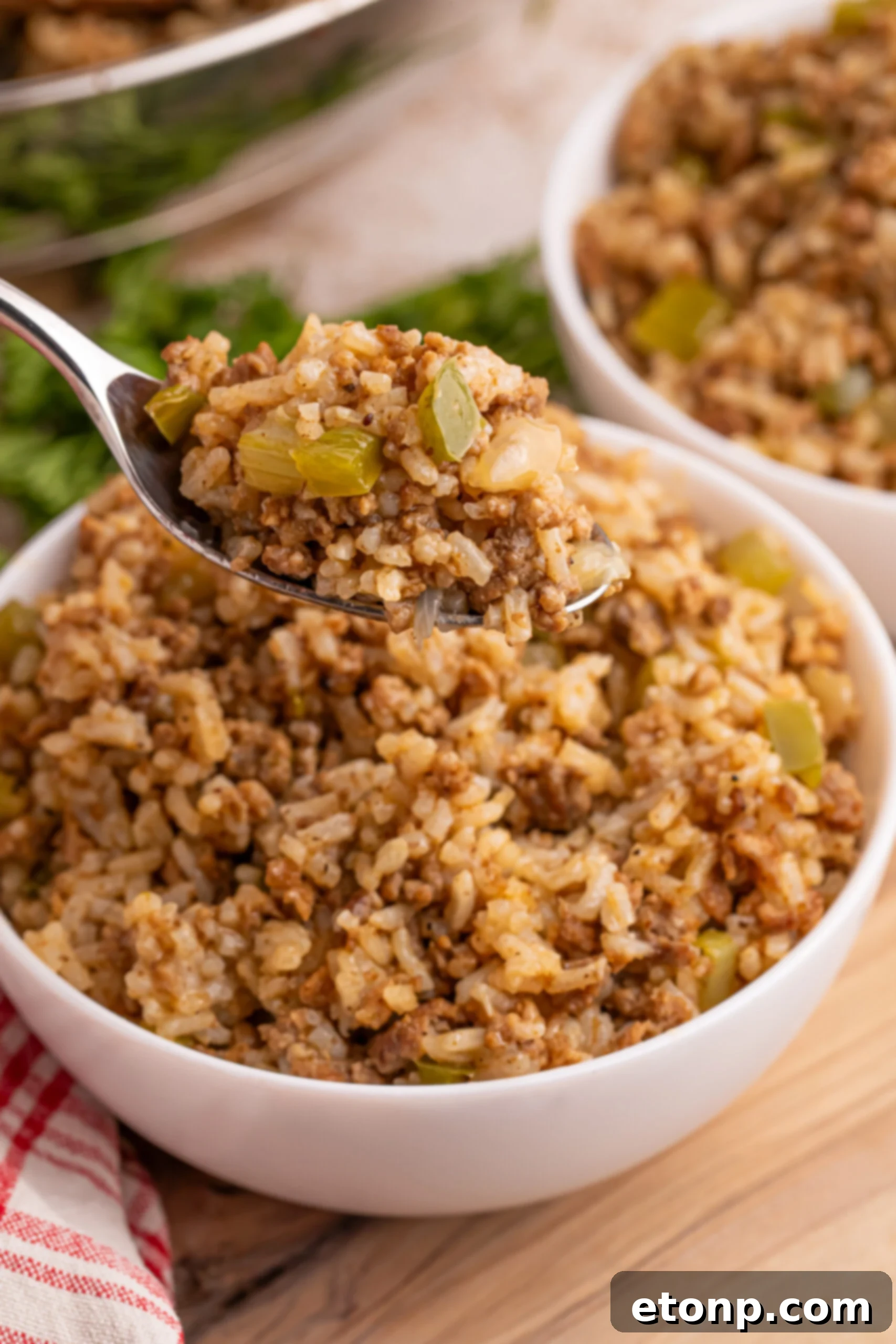 Cajun Dirty Rice 2 Dirty Rice in a white bowl sitting on a table with a spoon lifting up a bite