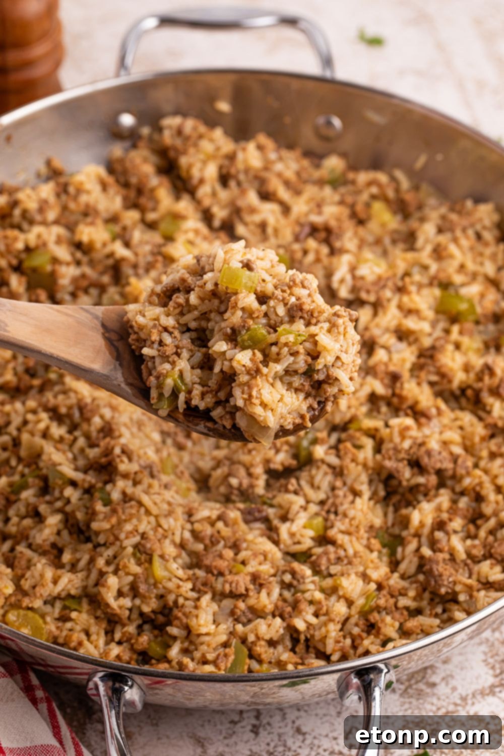 Cajun Dirty Rice 15 Dirty Rice in a pan with a scoop on a wooden spoon above the pan