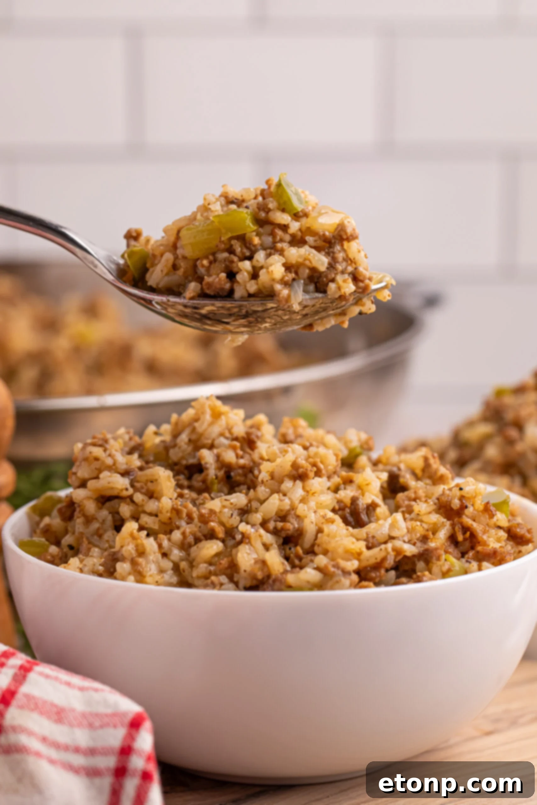 Cajun Dirty Rice 18 Dirty Rice in a white bowl sitting on a table with a spoon lifting up a bite