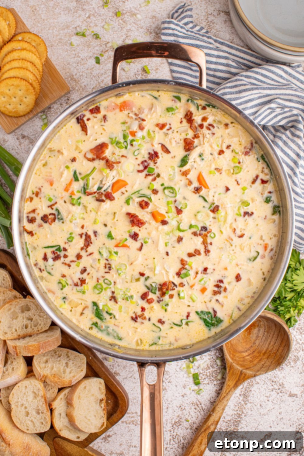 Creamy Ranch Chicken Soup 11 overhead look of Crack Chicken Soup in a pan on table with sliced bread around it, herbs and a wooden spoon
