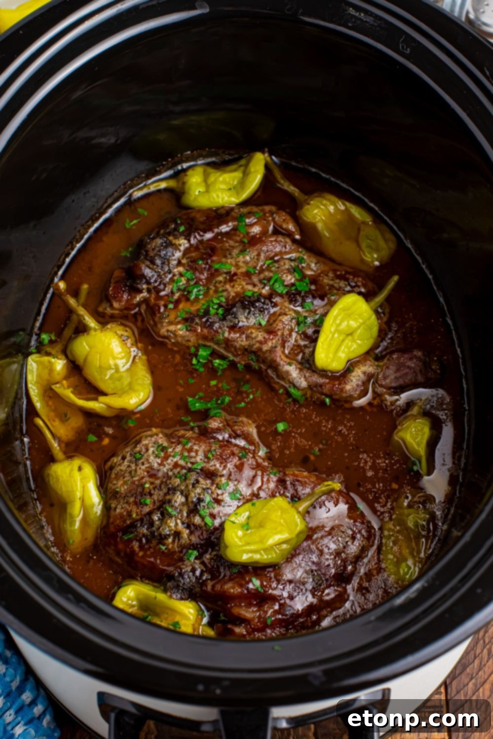 Slow Cooker Mississippi Ribeye Steaks sitting in a crockpot wih peppers on top