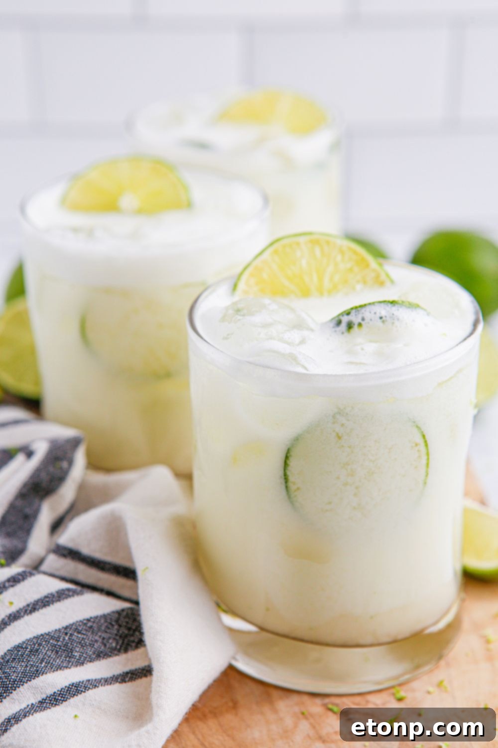 three glasses of Brazilian Limeade sitting on table with a towel and limes around it on table 