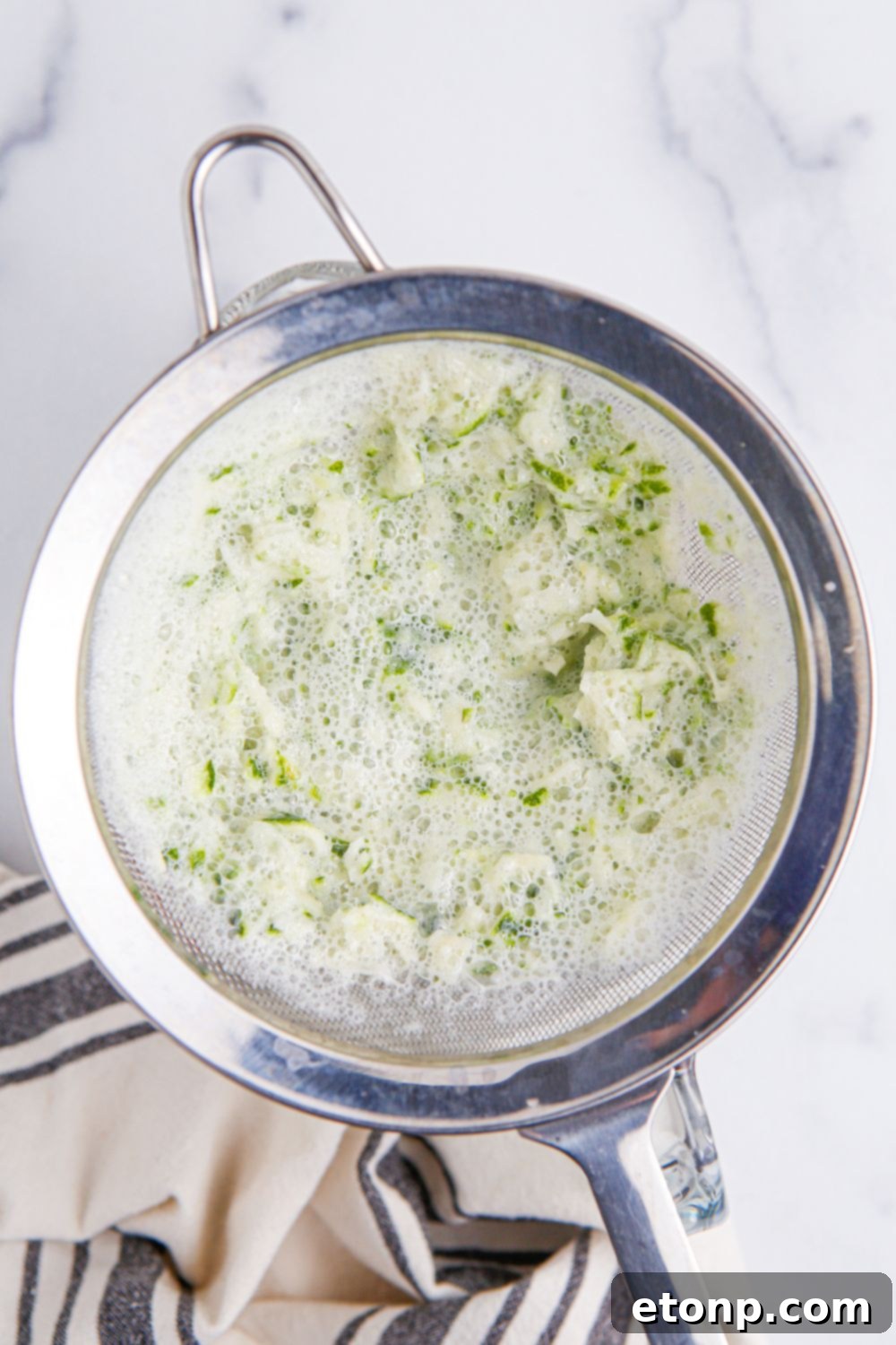 creamy limemade mixture being strained from a strainer 