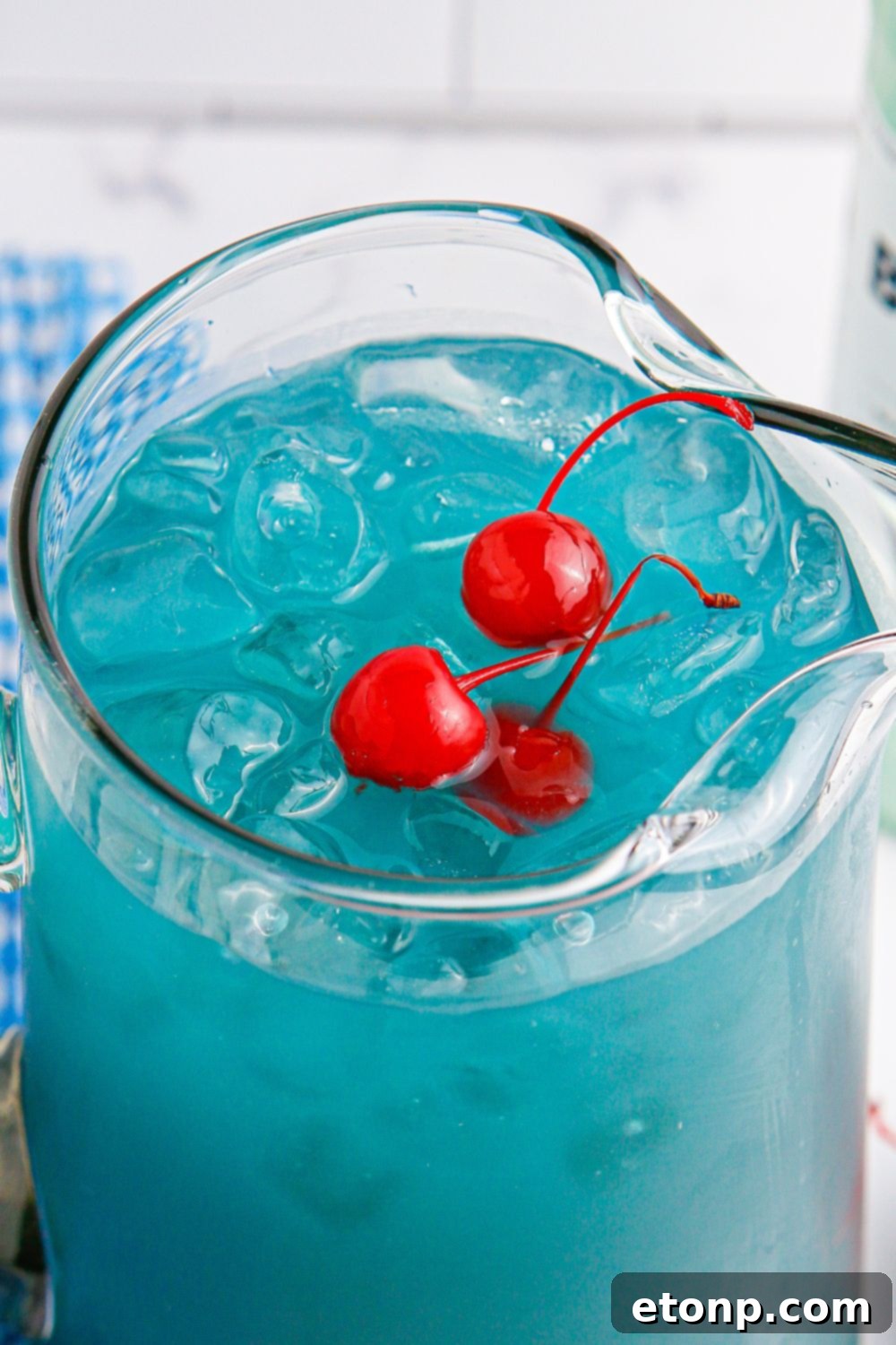 Hawaiian Punch with a few cherries sitting on top of ice in a glass pitcher