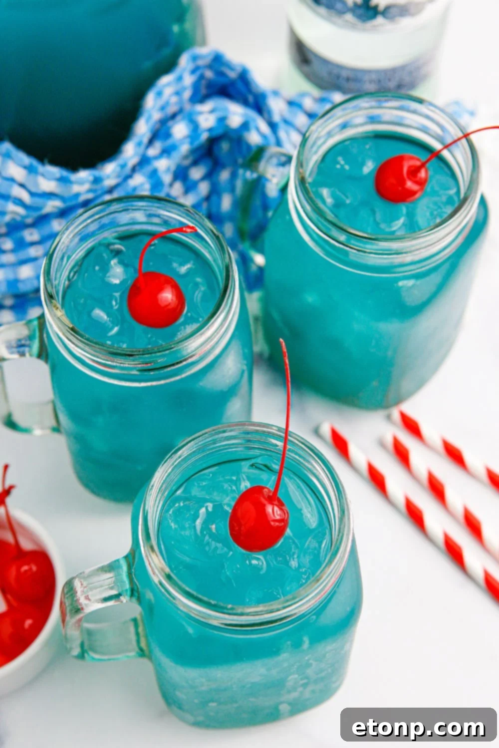 Glasses of blue cocktails with a cherry on the top of the ice in each glass