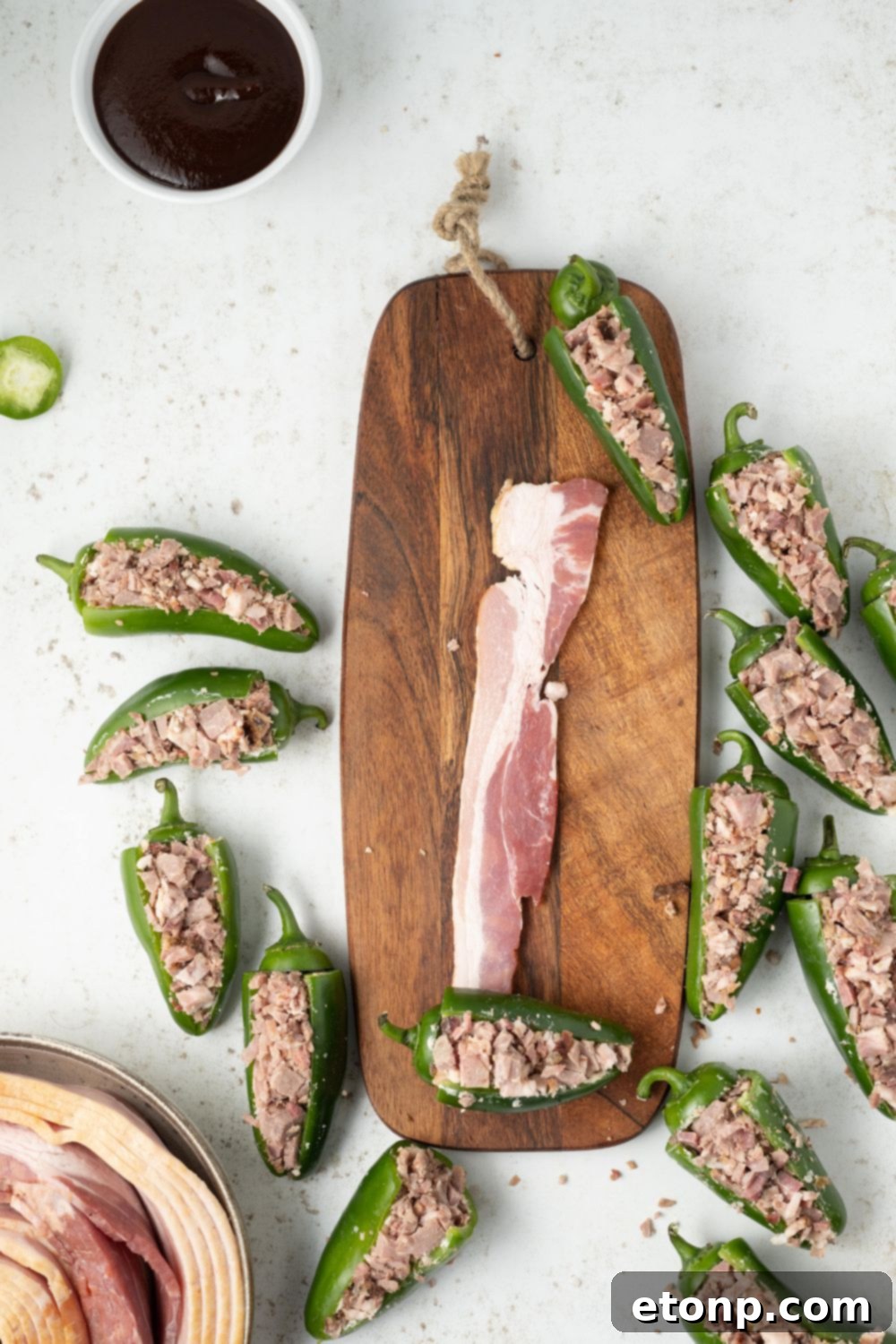 Slices of raw thick-cut bacon on a cutting board, surrounded by partially assembled Texas Twinkies